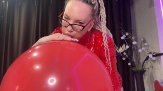 Looner-Mädchen mit Brille und rotem PVC-Kleid blasen GROSSEN roten Ballon und platzen mit. DM, um voll zu werden